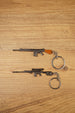 SA58 FAL battle rifle keychains in base and modded styles on a wooden surface, showing metal keyrings and detailed gunmetal finishes