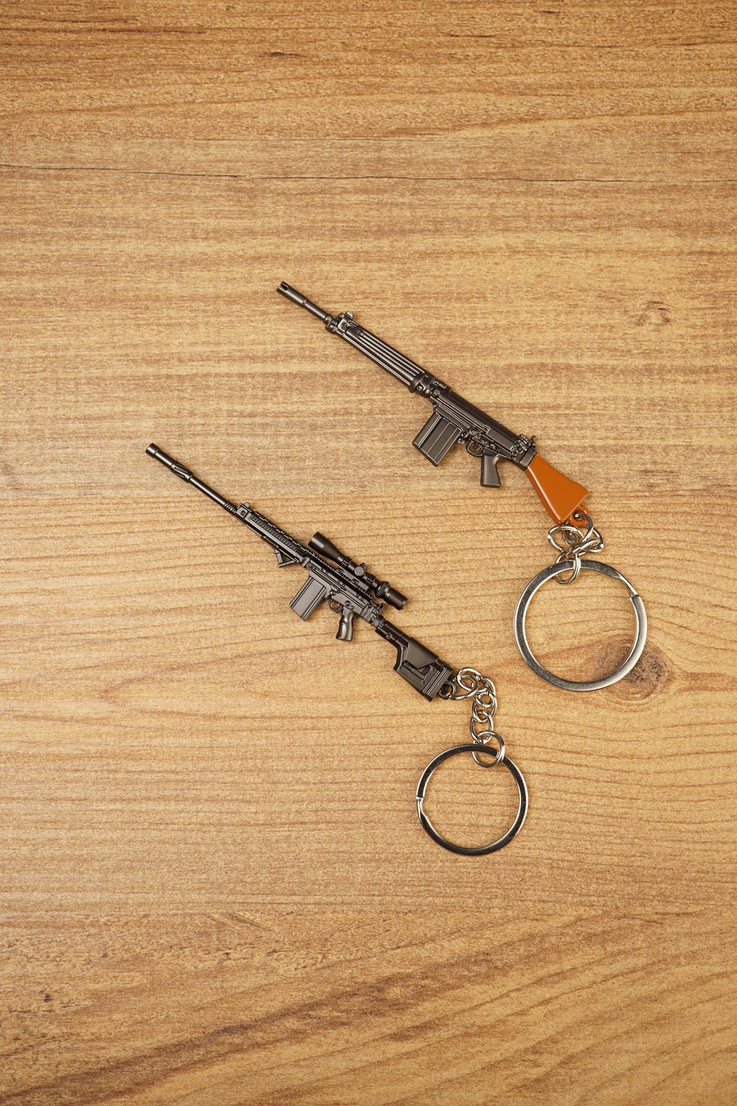 Two SA58 FAL rifle keychains displayed diagonally on wood, featuring base and tactical modded versions for FPS gamer collectors