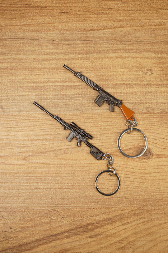 Two SA58 FAL rifle keychains displayed diagonally on wood, featuring base and tactical modded versions for FPS gamer collectors