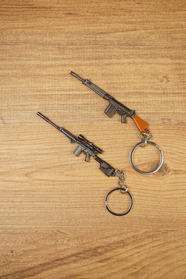Two SA58 FAL rifle keychains displayed diagonally on wood, featuring base and tactical modded versions for FPS gamer collectors