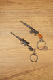 Two SA58 FAL rifle keychains displayed diagonally on wood, featuring base and tactical modded versions for FPS gamer collectors