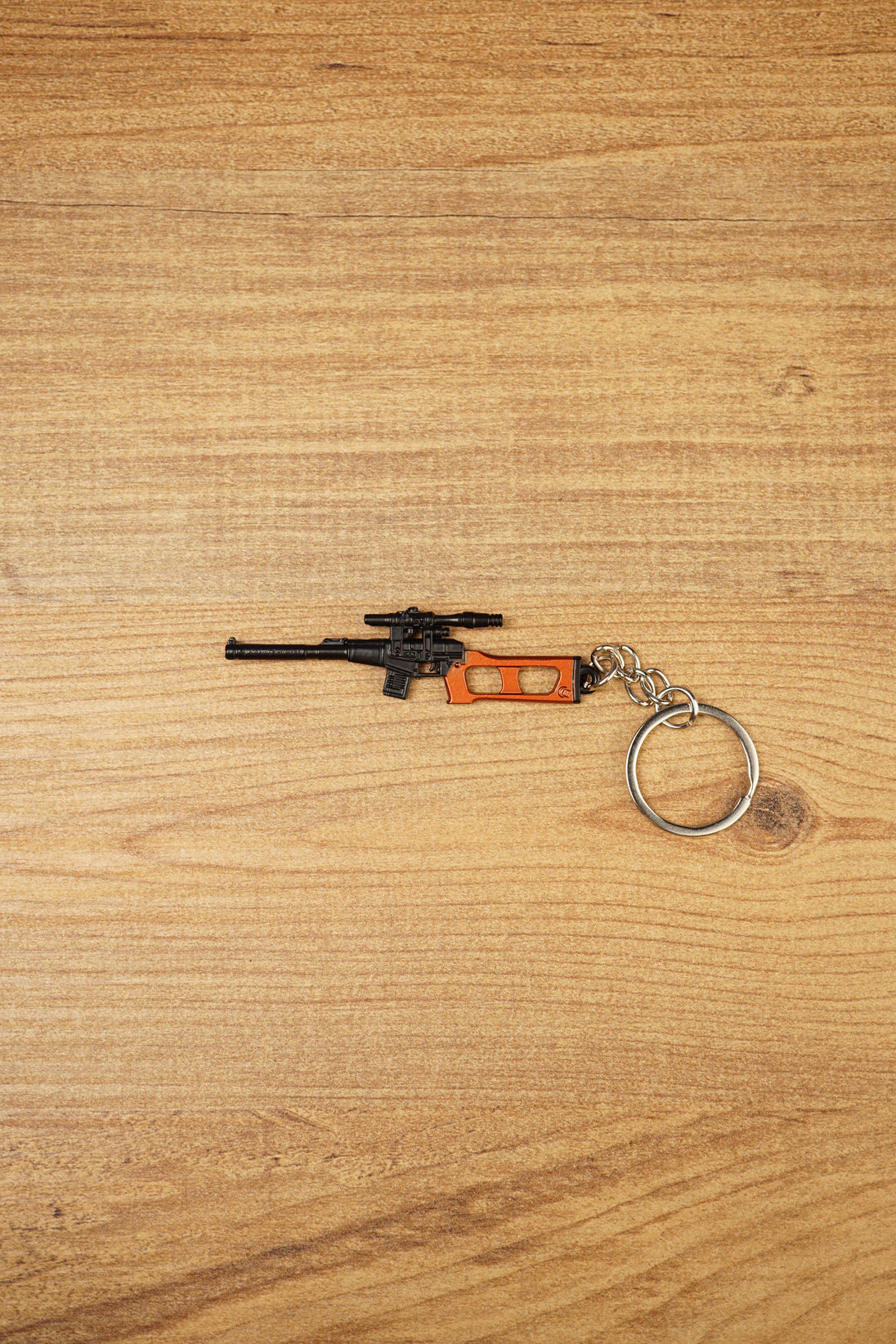 Scoped VSS Vintorez style rifle keychain with orange stock detail and silver keyring shown on a wooden surface
