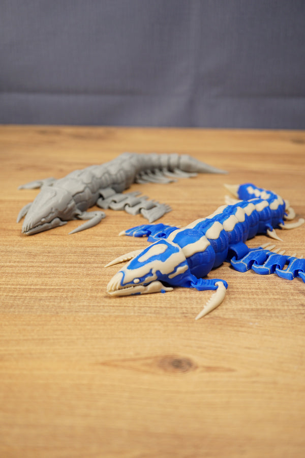 Shiver Leviathan collectible figure posed on a wooden surface with a grey creature model in the background for comparison.