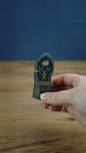 Hand holding a small personalized Valheim-inspired tombstone with orange rune details and YOURNAME text on the front.