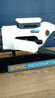 Close side view of Subnautica 2 Sonic Resonator replica showing the white body panels, side control, cyan detail and Sonic Resonator display stand