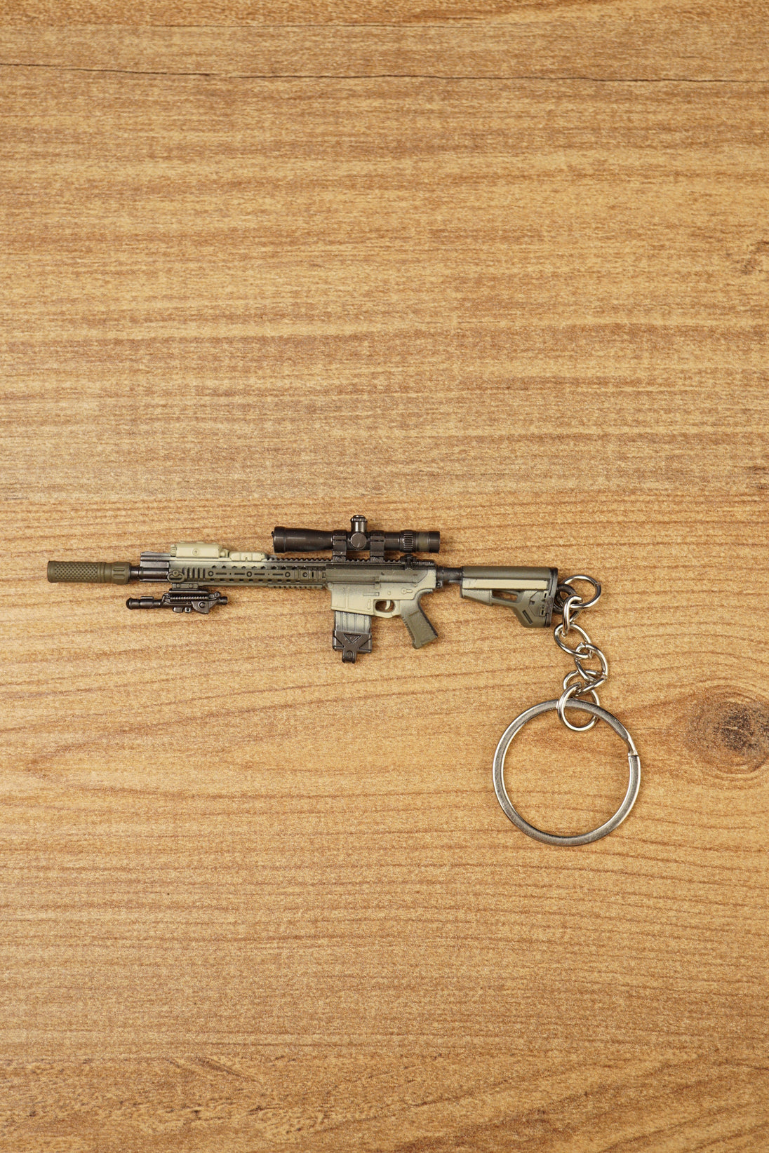 SR-25 DMR rifle keychain laid flat on a wooden surface, showing the tan tactical body, scope, magazine, stock, and metal keyring attachment