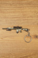 SR-25 DMR rifle keychain laid flat on a wooden surface, showing the tan tactical body, scope, magazine, stock, and metal keyring attachment