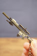 Close-up of SR-25 DMR rifle keychain held by hand, highlighting the tan rifle body, scope, barrel detail, stock, and metal keychain loop.