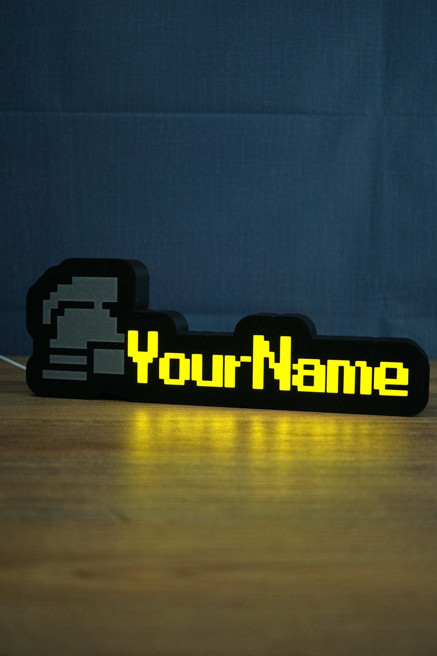 Illuminated standard ironman nameplate glowing in the dark with a grey helmet icon, yellow lettering, and soft reflection on the tabletop.