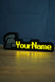 Illuminated standard ironman nameplate glowing in the dark with a grey helmet icon, yellow lettering, and soft reflection on the tabletop.