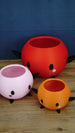 Angled group photo of pink, orange, and red Stardew Valley Junimo planter pots arranged together on a wooden tabletop with a blue backdrop.