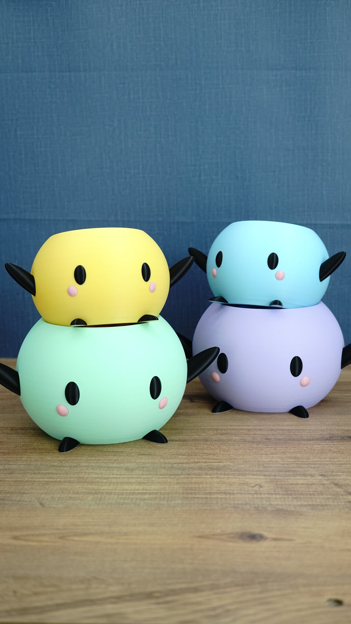 Four colorful Stardew Valley Junimo planter pots stacked in mint green, yellow, lavender, and blue on a wooden tabletop
