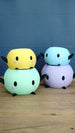 Four colorful Stardew Valley Junimo planter pots stacked in mint green, yellow, lavender, and blue on a wooden tabletop