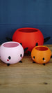 Three Stardew Valley Junimo planter pots in pink, orange, and red, showing different sizes with black arms, black feet, and cute face details.