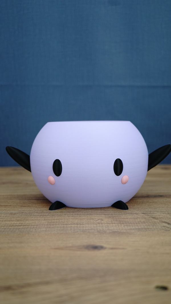 Purple Stardew Valley Junimo planter pot with black arms, feet, eyes, and pink cheeks, shown from the front on a wooden tabletop.