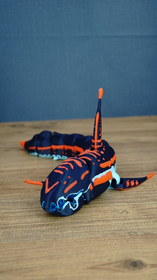 Articulated Marrowbreach Subnautica 2 figure in dark blue with orange markings, white details, blue mouth parts, fins, and segmented body on a wooden tabletop.