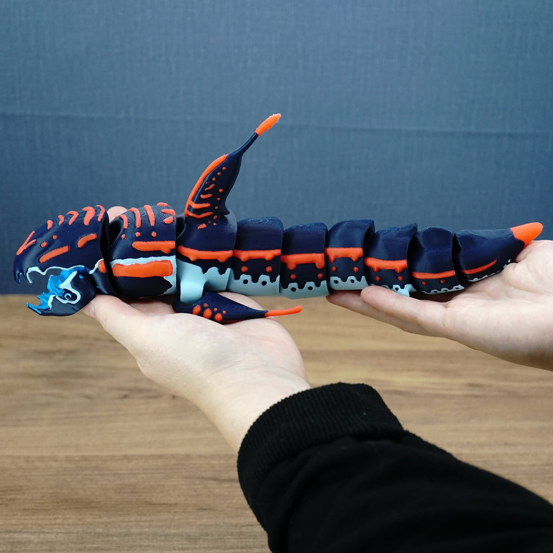 Full side view of an articulated Subnautica Marrowbreach figure held in two hands, showing its long segmented body, fins, tail, and orange striped details.