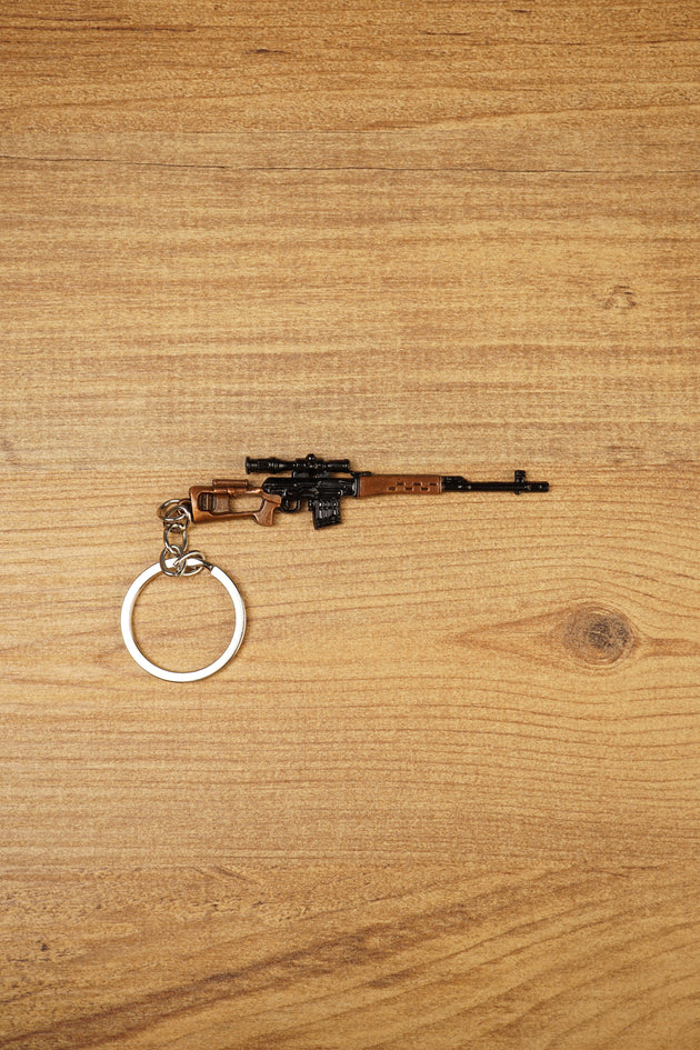 SVDS rifle metal keyring laid flat on a wooden surface, showing the long barrel, scope, bronze stock and split keyring attachment