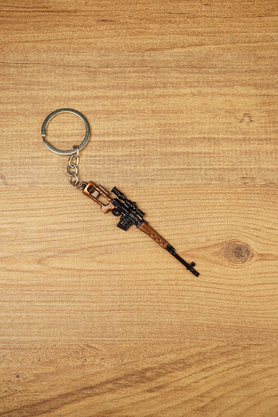SVDS-style sniper rifle metal keyring displayed diagonally on a wooden table, ideal as a gamer gift or collectible accessory