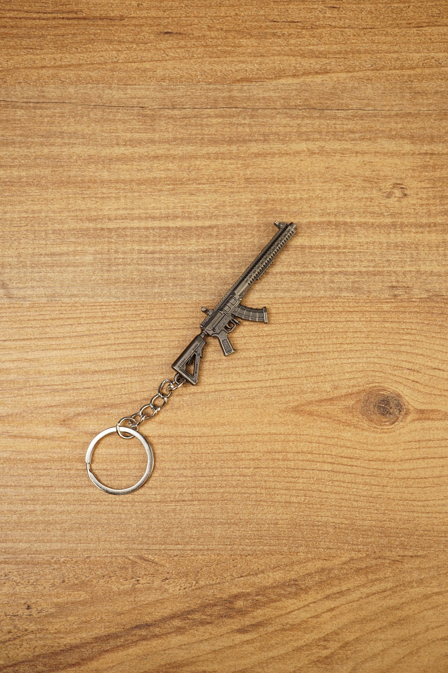 Angled MK47-style metal rifle keychain on wood, ideal as a tactical FPS gamer gift, backpack charm or collectible accessory