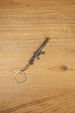 Angled MK47-style metal rifle keychain on wood, ideal as a tactical FPS gamer gift, backpack charm or collectible accessory
