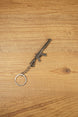 Angled MK47-style metal rifle keychain on wood, ideal as a tactical FPS gamer gift, backpack charm or collectible accessory