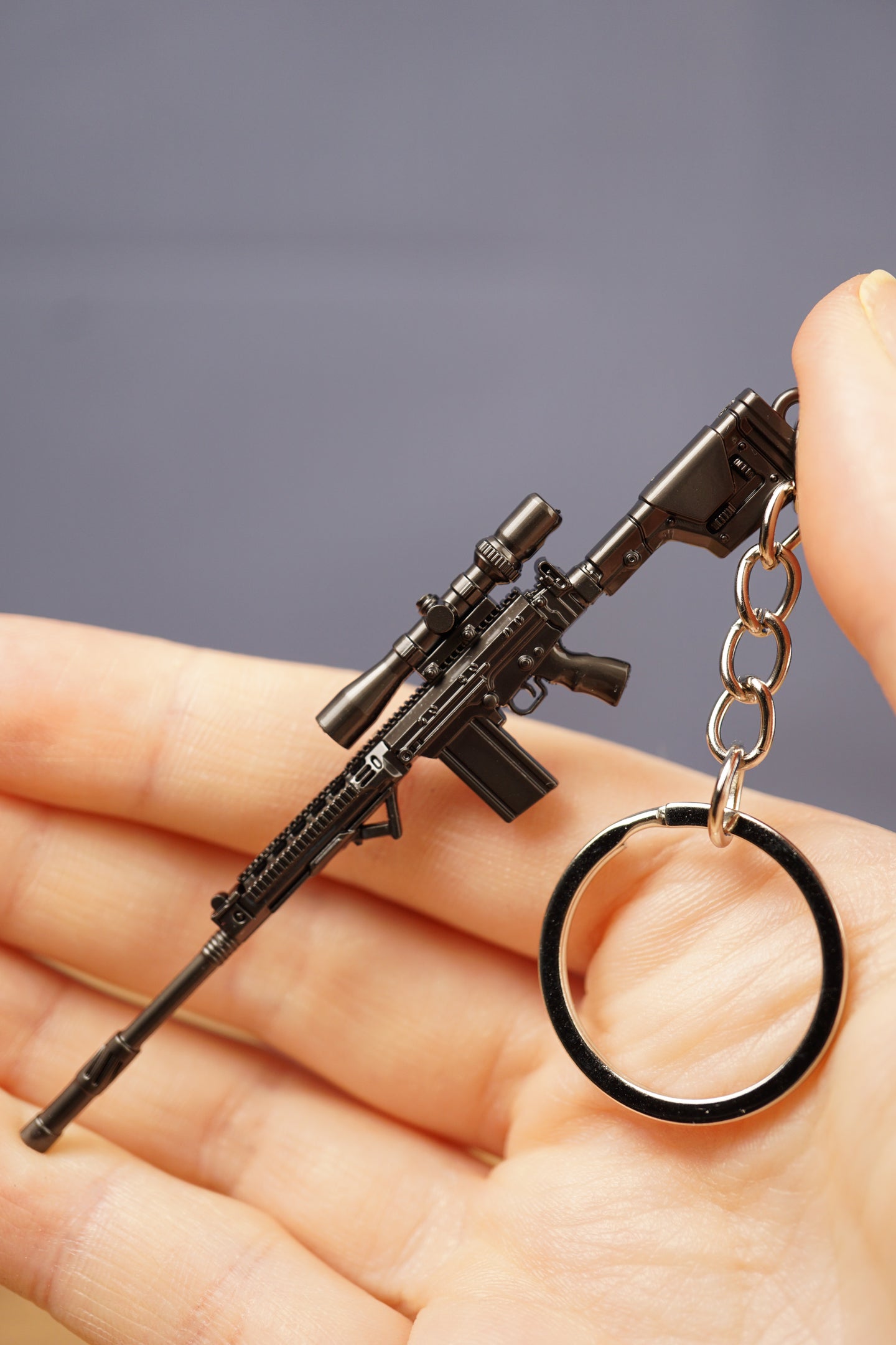 Modded tactical rifle keychain in hand with scope-style accessory, dark metal finish, magazine detail and circular keyring