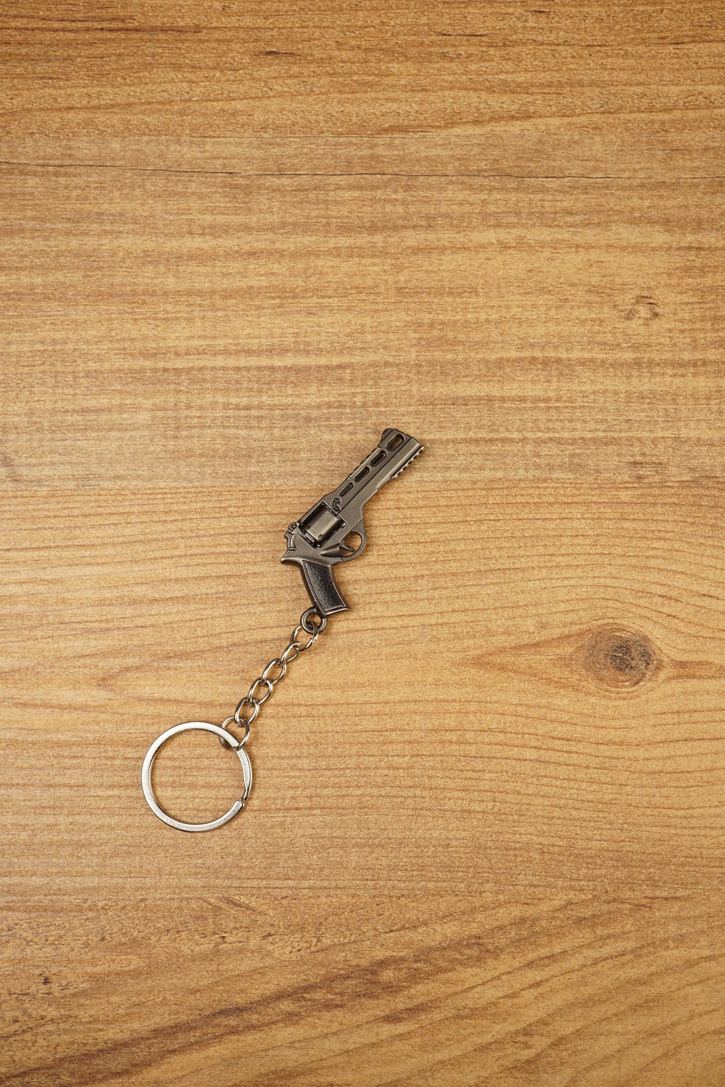 Angled tactical revolver keychain on wood showing the compact gunmetal body, black handle, and keyring chain for gaming fans