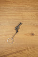 Angled tactical revolver keychain on wood showing the compact gunmetal body, black handle, and keyring chain for gaming fans