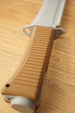 Close-up of the brown textured handle and gray guard on a 3D-printed machete replica lying on a wooden tabletop.