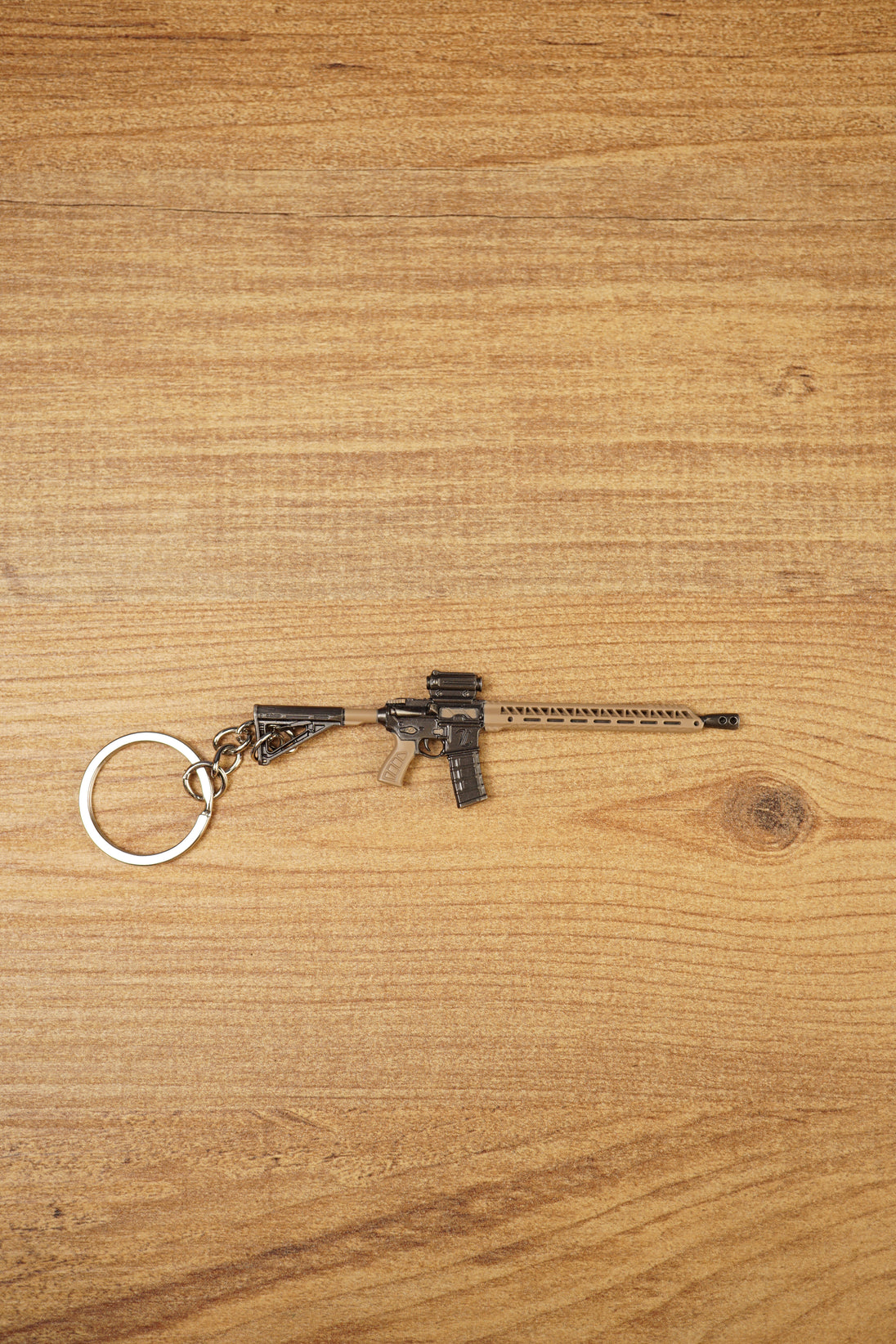 Tan and black long rifle keychain with metal key loop displayed on a wooden tabletop for tactical shooter fans.