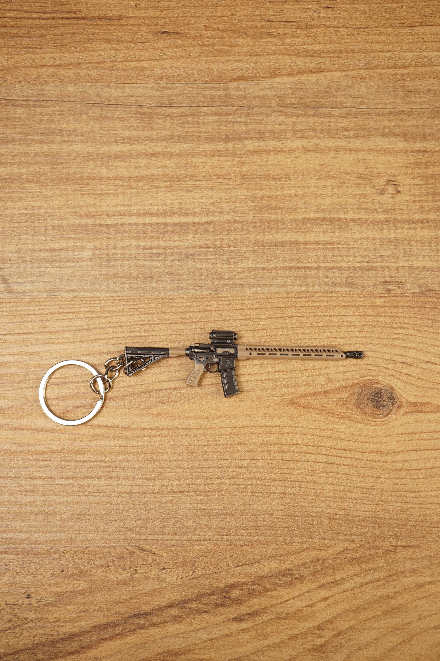 Tan and black long rifle keychain with metal key loop displayed on a wooden tabletop for tactical shooter fans.
