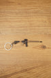 Tan and black long rifle keychain with metal key loop displayed on a wooden tabletop for tactical shooter fans.