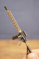 Close-up of tan and black tactical rifle keyring held by fingers, showing long barrel, sight and magazine details.