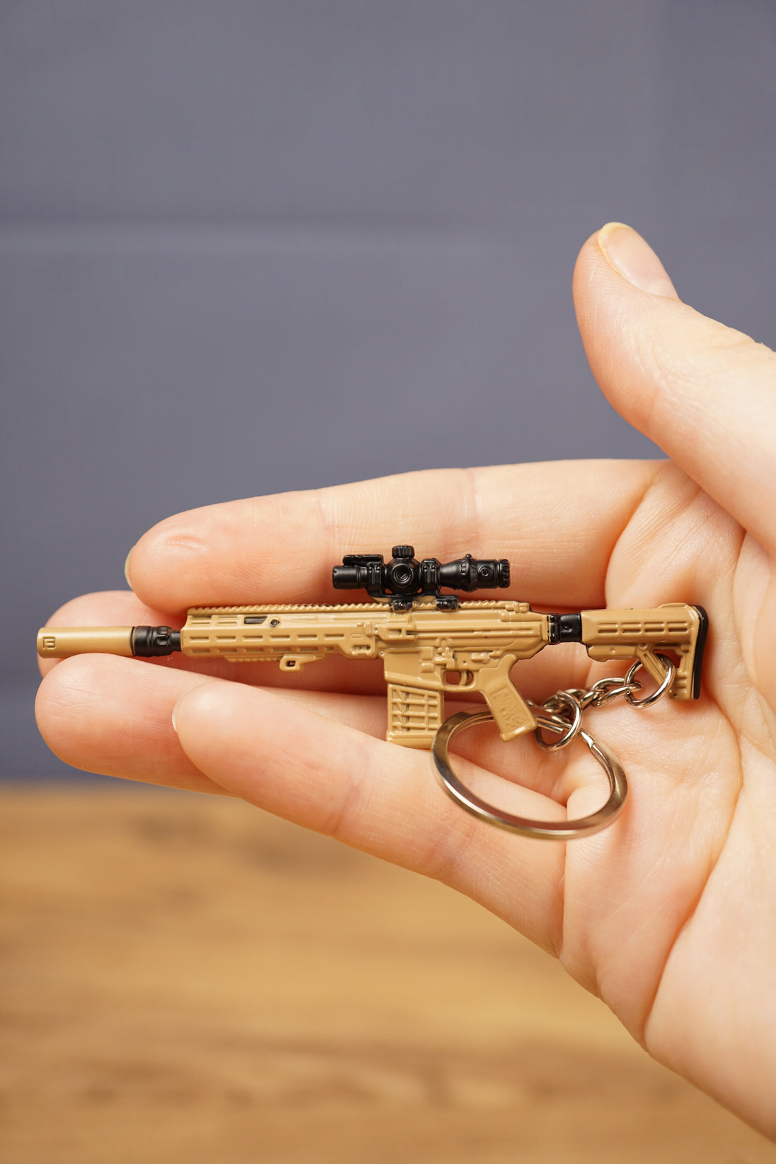 Tan tactical rifle keyring with black optic, stock and barrel details resting in hand, a compact collectible gift for shooter game fans