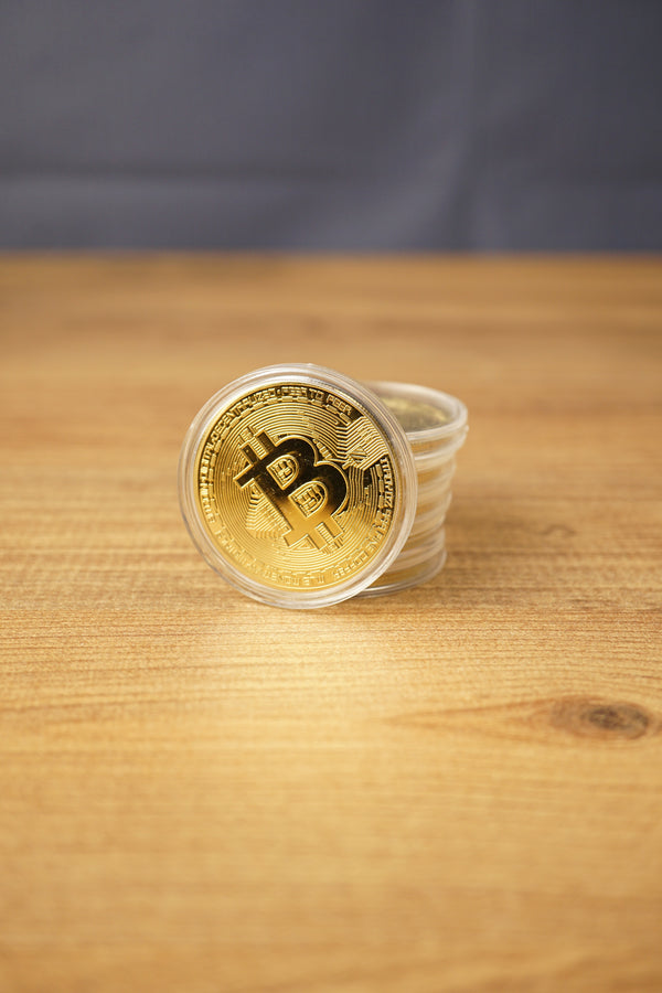 Stack of gold Bitcoin replica coins in clear plastic capsules, with one coin standing upright on a wooden table.