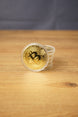 Stack of gold Bitcoin replica coins in clear plastic capsules, with one coin standing upright on a wooden table.