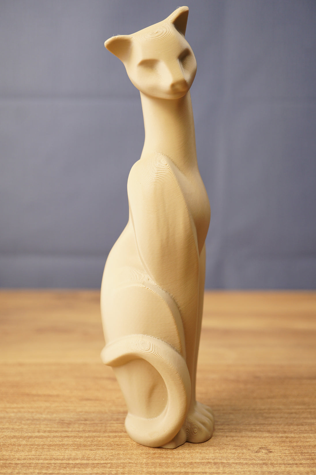 Tall Tarkov inspired cat figurine replica displayed on a wooden tabletop, with beige finish, elegant seated pose, and curved tail design.