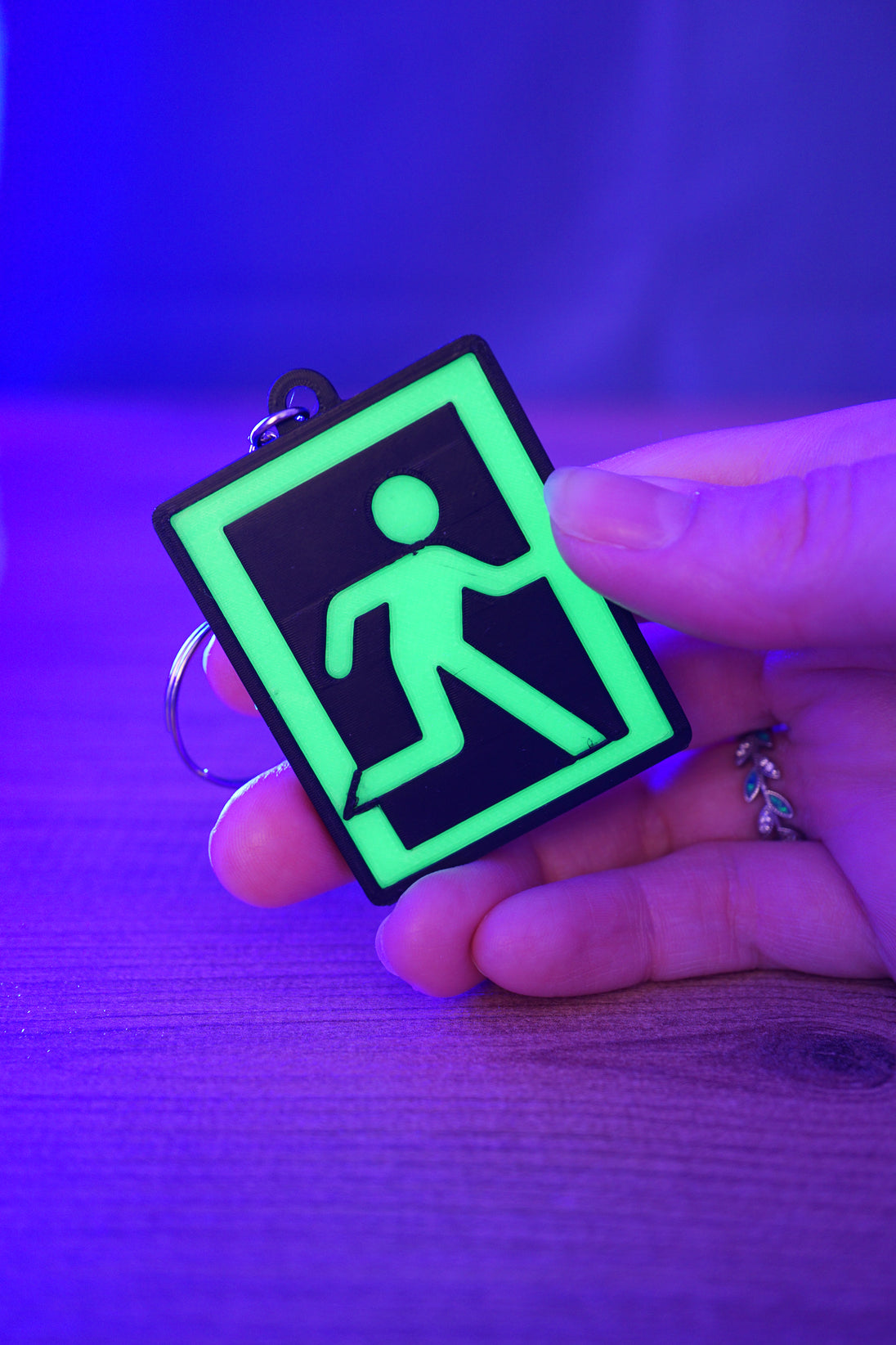 Glow-in-the-dark Tarkov extraction keyring held in hand under blue and purple UV lighting, with a bright green running figure icon and black border.