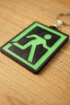 Close-up angled view of a Tarkov extraction keyring on a wooden surface, highlighting the green figure, black border, and layered 3D printed texture.