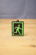 Tarkov inspired extraction keyring standing upright on a wooden tabletop, featuring a green running figure sign with black background and frame.