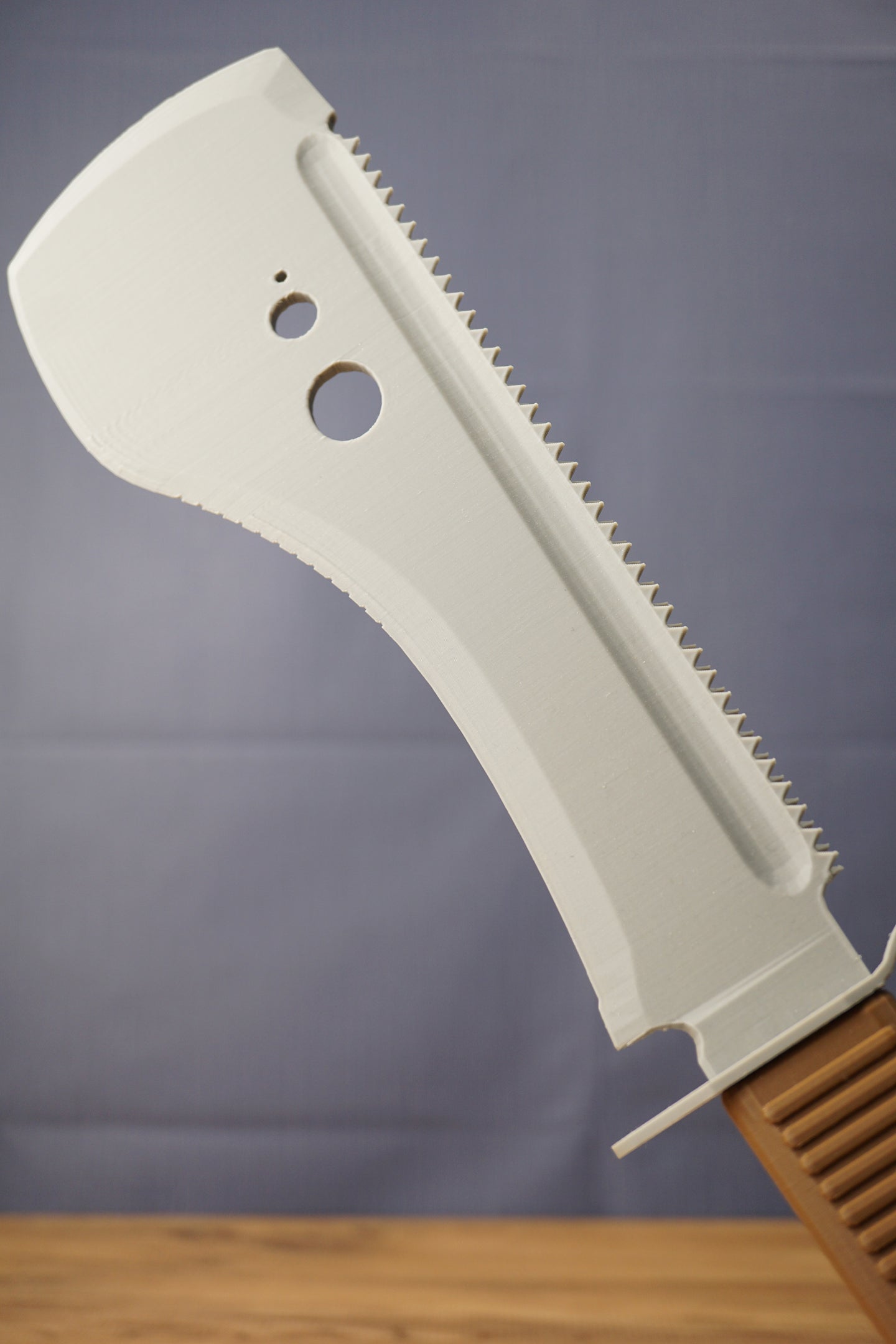Close-up of a gray 3D-printed machete replica blade, showing serrated detailing, circular cutouts, and raised center ridge.