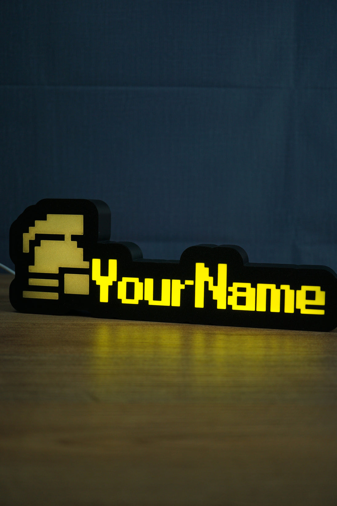 Lit ultimate ironman nameplate with a silver helmet icon, yellow RuneScape-style lettering, and a soft glow reflected on the tabletop.