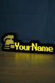 Lit ultimate ironman nameplate with a silver helmet icon, yellow RuneScape-style lettering, and a soft glow reflected on the tabletop.