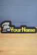 Ultimate ironman RuneScape-style nameplate with a silver helmet icon, bright yellow custom text, and black border displayed on a desk.