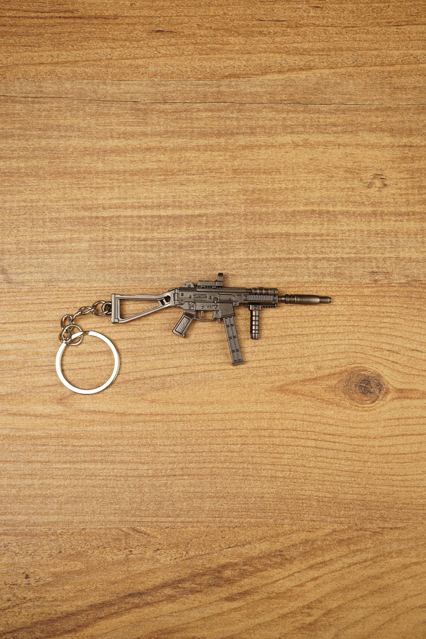 UMP45-style modded submachine gun keyring laid flat on a wooden surface, showing the metal SMG design with chain and key ring attached