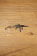 UMP45-style modded submachine gun keyring laid flat on a wooden surface, showing the metal SMG design with chain and key ring attached