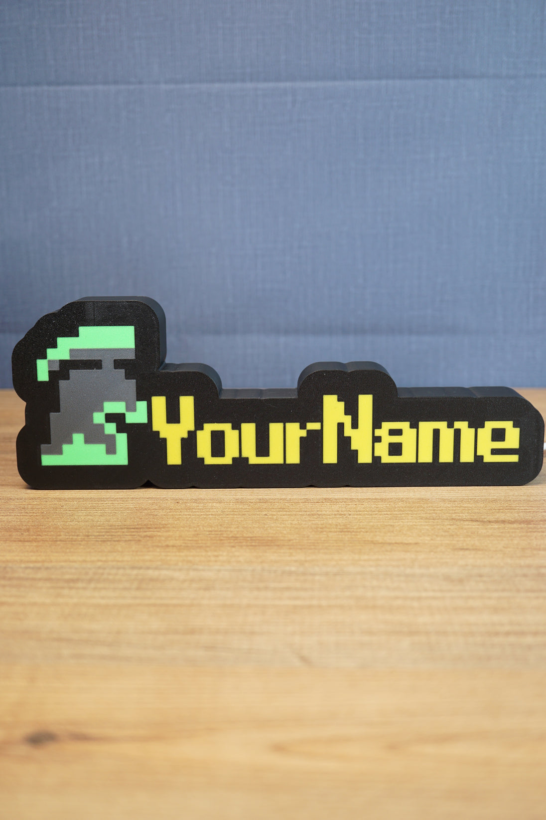 Personalized RuneScape-style nameplate featuring an unranked group ironman helmet icon with green and grey detailing and yellow custom lettering on a desk.