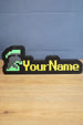 Personalized RuneScape-style nameplate featuring an unranked group ironman helmet icon with green and grey detailing and yellow custom lettering on a desk.
