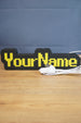 Custom USB-powered YourName LED sign with RuneScape-style font, yellow lettering, and black casing on a wooden desk.